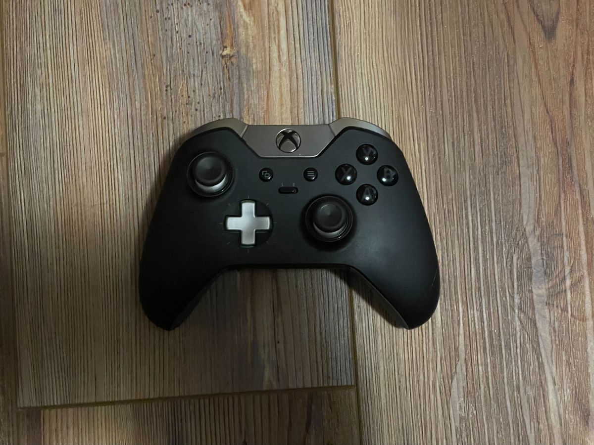 An Xbox Elite Controller Series 1 sits on a wooden floor