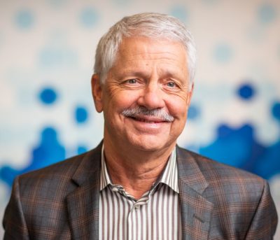 head shot by Dr.  Barry Lumb, a man with a gray mustache wearing a gray striped shirt and suit jacket