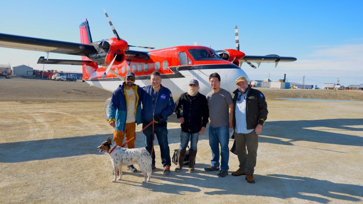 Members of the Month on Mars expedition stand next to a small propeller aircraft.