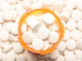 A prescription bottle filled with pills surrounded by several of the same pills.