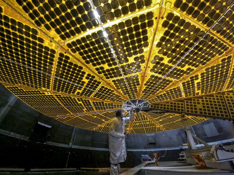 NASA troubleshoots Lucy: Large golden solar array with man in white protective suit standing under it.