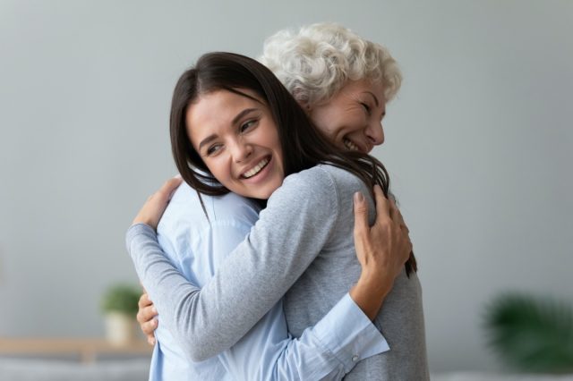 Happy granddaughter of young lady adult daughter hugging old retired grandmother cuddling