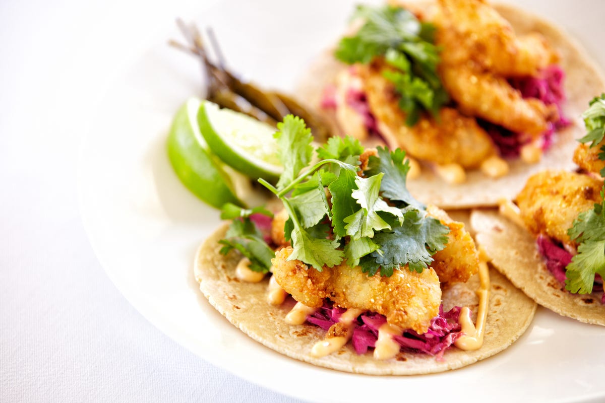 Fish tacos on a plate with corn tortillas and fresh cilantro.