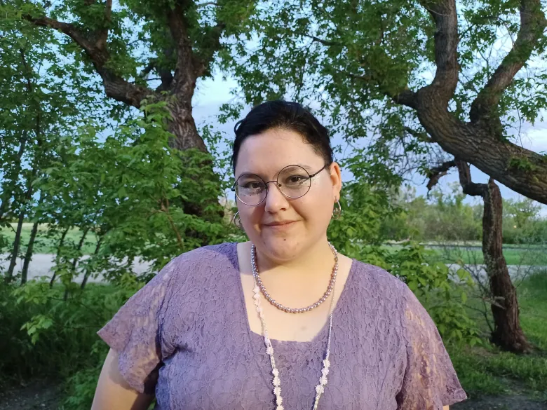 Ell Bird poses in a grove of trees.  You work with queer youth in Moose Jaw, Sask.