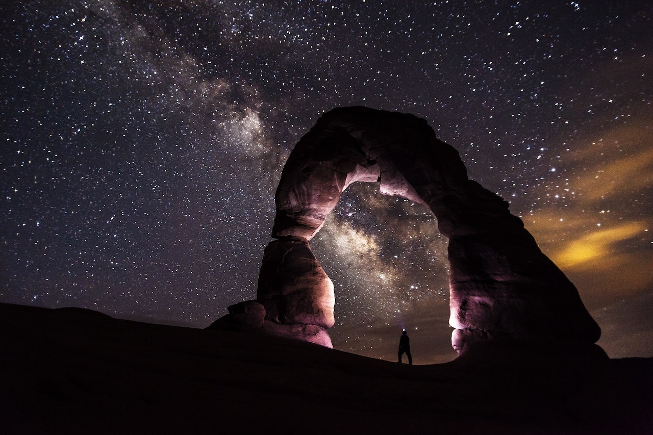 A person standing under a rock formation on a starry night