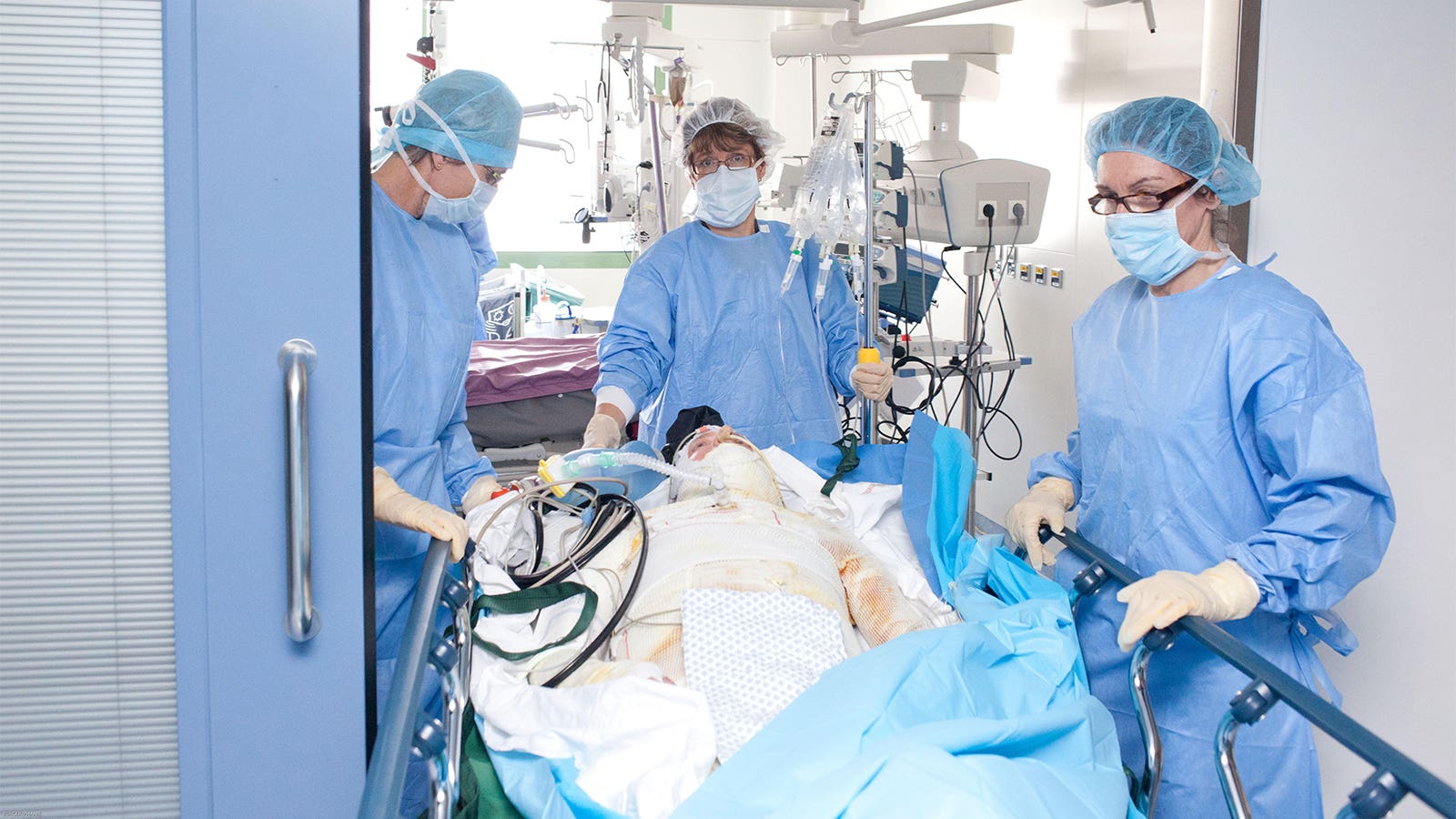 A photo of a burn patient wrapped in bandages being wheeled out of the operating room by three nurses.