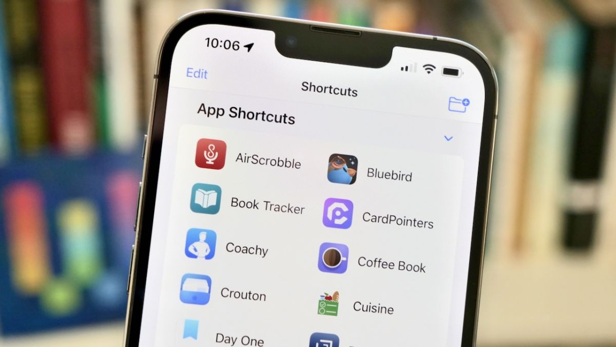 Photograph of App Shortcuts on an iPhone with the logo of Workflow, the previous version of Shortcuts, visible in the background on a bookshelf.