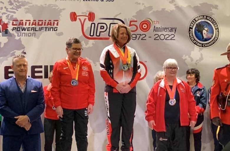 Three people with medals around their necks stand on a pedestal.