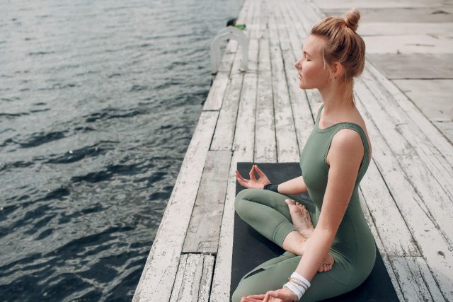 Woman relaxing while doing yoga near the water