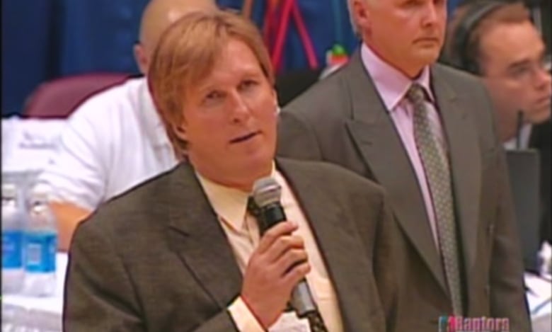 A man holding a microphone stands on a basketball court. 