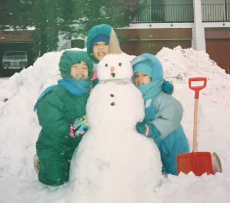 Three girls in snow suits hug a snowman.