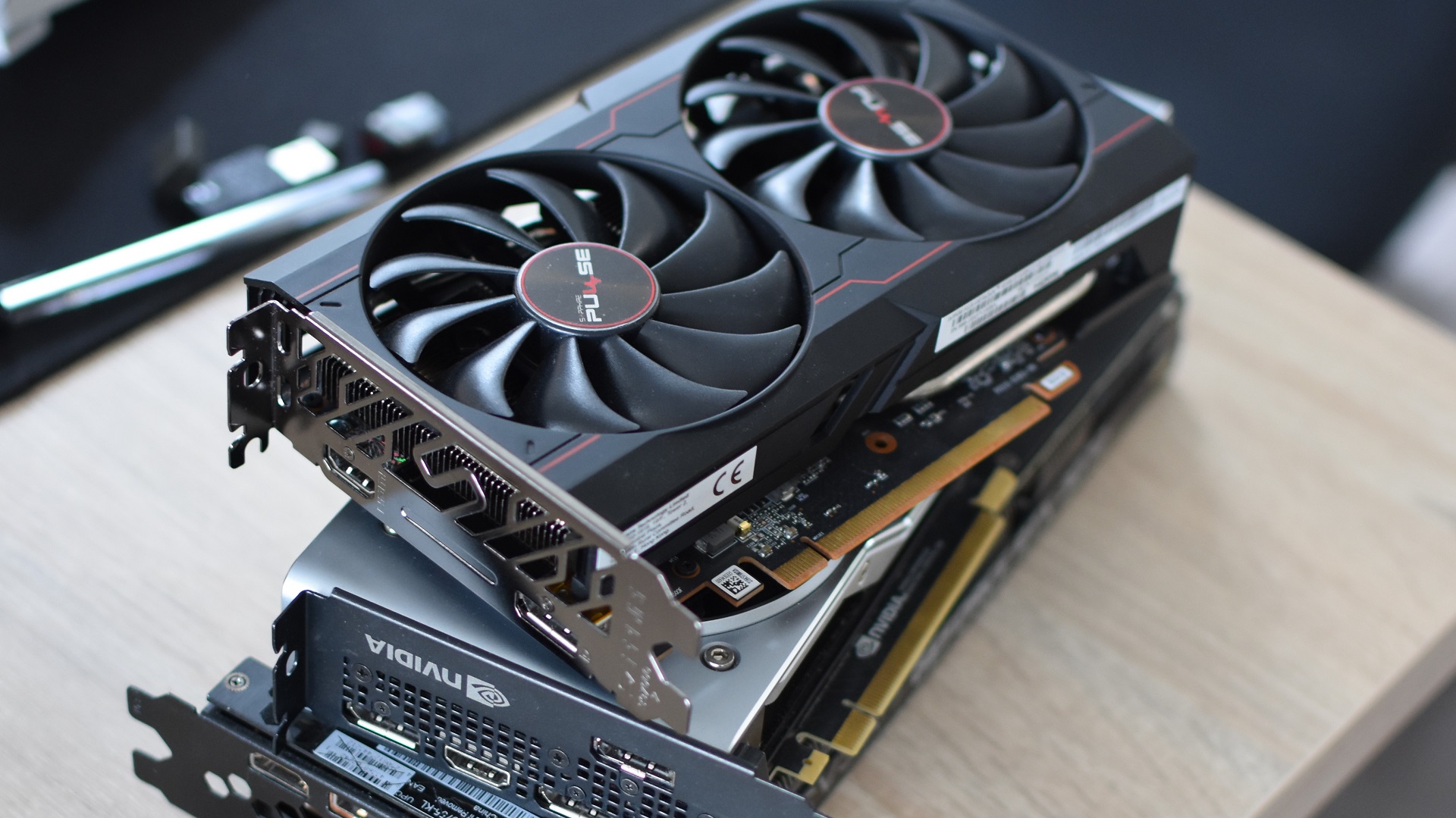 A stack of various Nvidia and AMD graphics cards piled on a desk.