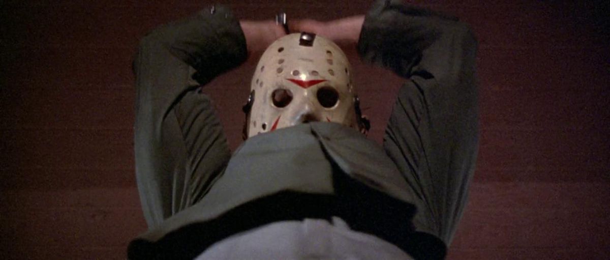 Jason Voorhees, wearing his signature hockey mask, holds both hands above his head ready to cut someone in Friday the 13th, Part III.