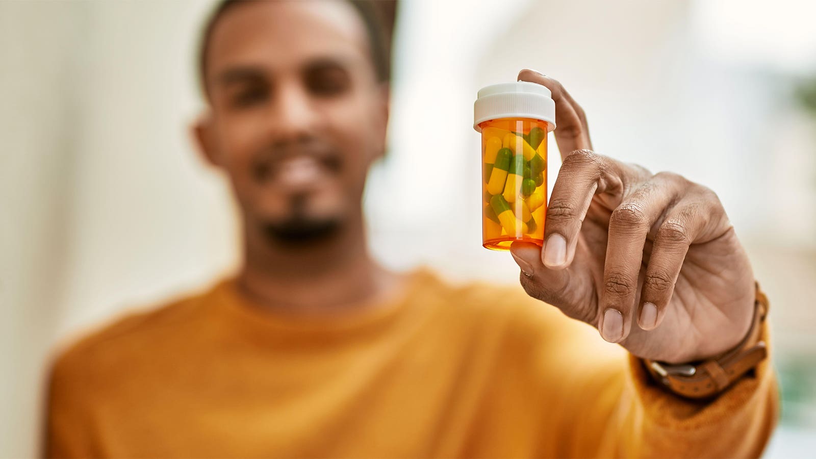 A photo of a smiling man holding out a prescription bottle of capsules.