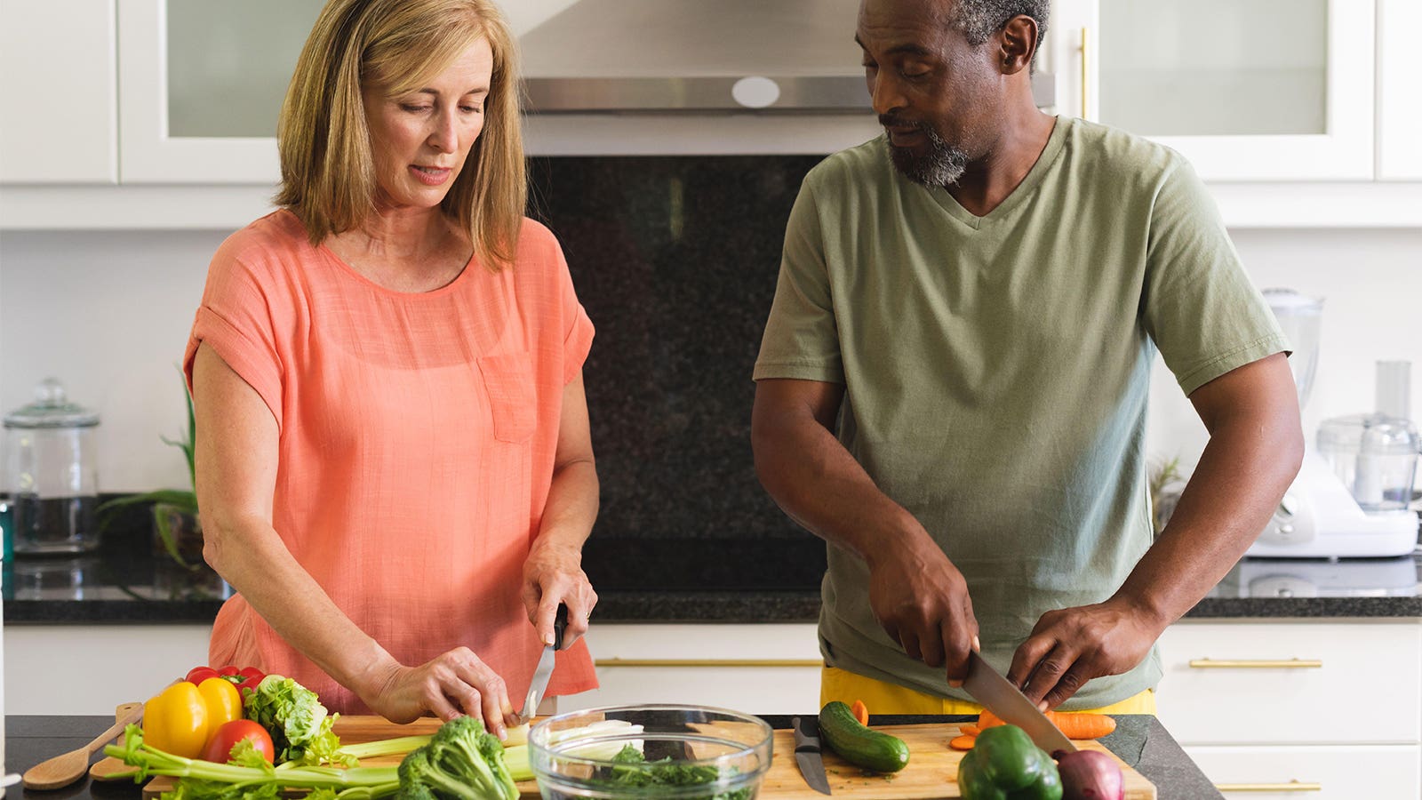 A photo of a mature couple chopping vegetables in the kitchen.