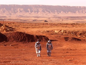 A pair of astronauts walk in space suits during a training mission for the planet Mars.